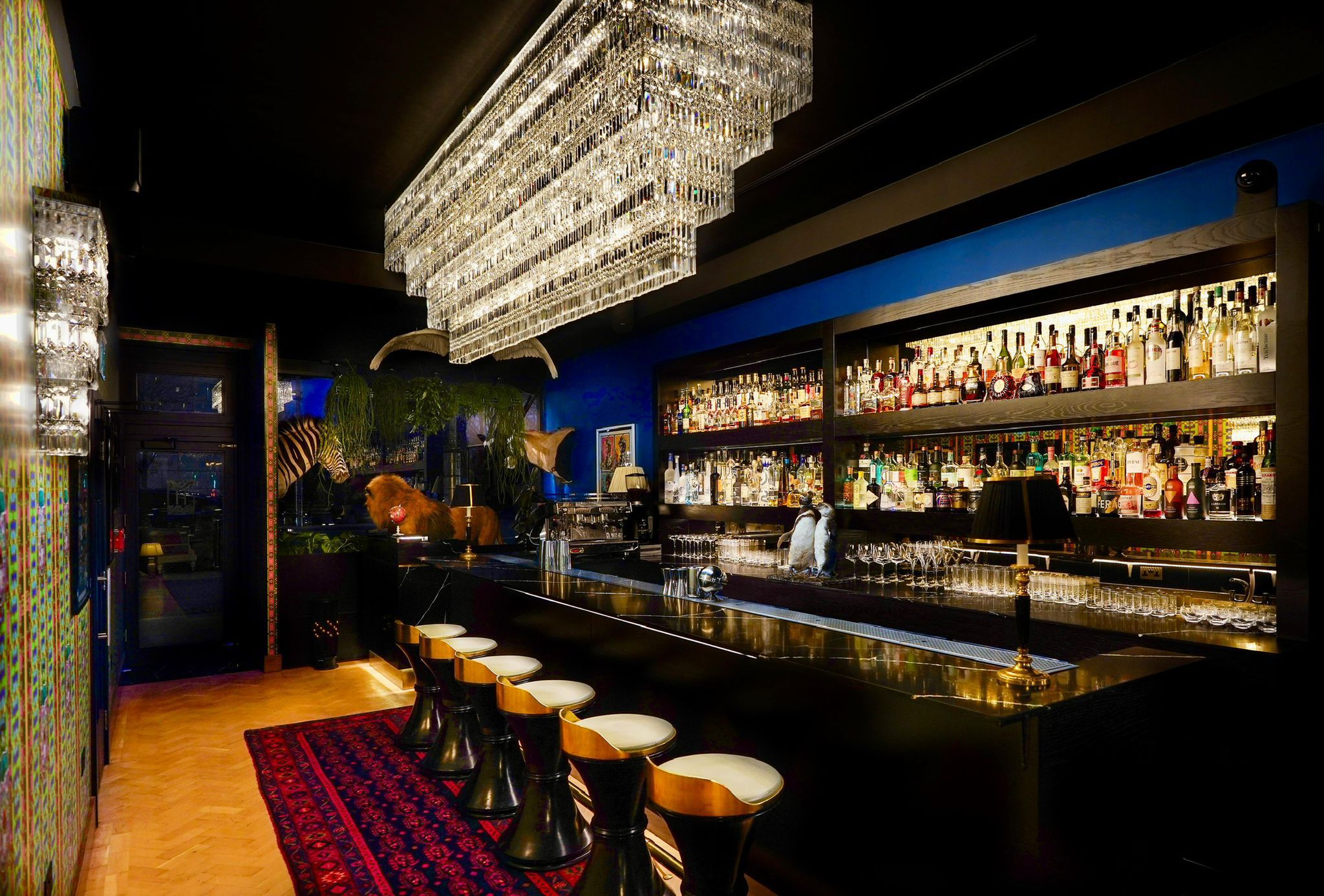 The HUX Kensington bar beneath its crystal chandelier, backed by a lit spirits display